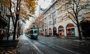 A tram travels down a leaf-strewn street in autumnal Zürich, Switzerland's urban landscape.