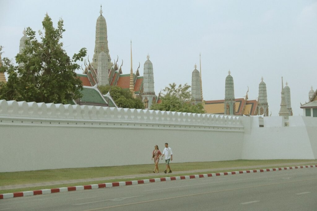 two people walking down a street past a white wall