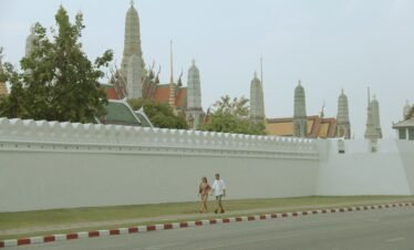 two people walking down a street past a white wall
