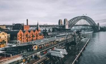 aerial photography of concrete buildings and bridge beside ocean under cloudy sky