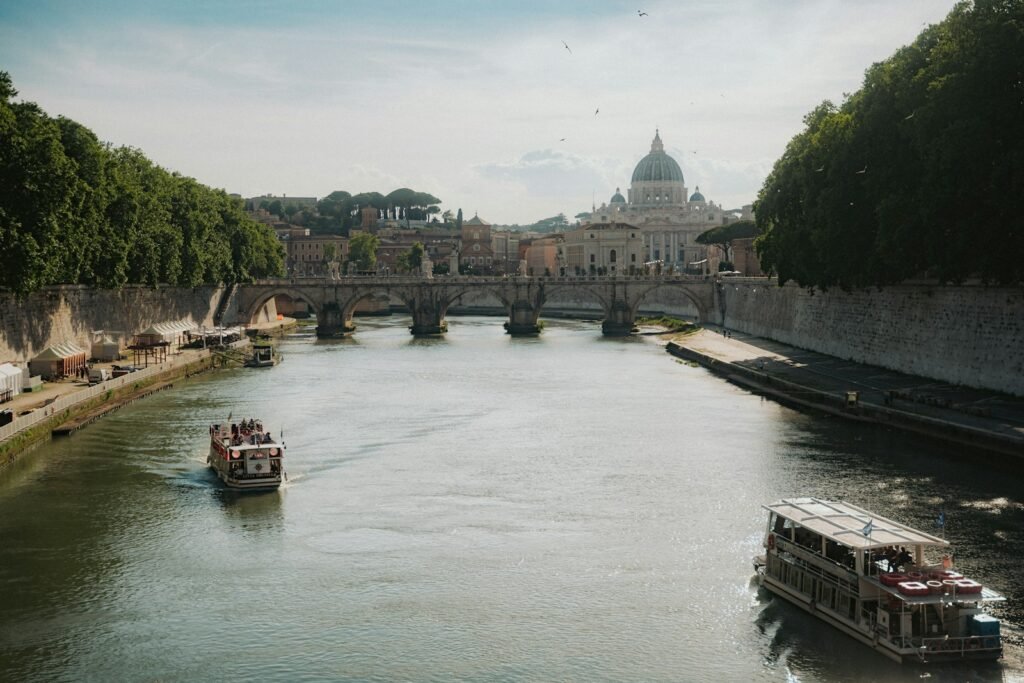 Boats travel a river with st. peter's basilica in view.
