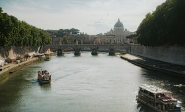 Boats travel a river with st. peter's basilica in view.