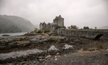 a stone castle on a hill with Eilean Donan in the background